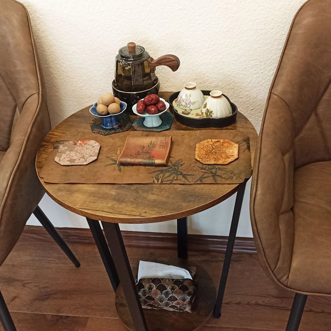 Ein runder Tisch mit Tee-Set, Schälchen, Kanne und Deko zwischen zwei braunen Stühlen.